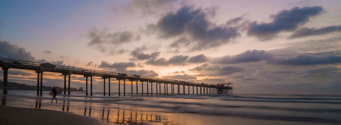 Scripps Pier at sunset with a surfer walking in front