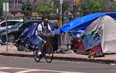 A man riding his bike through a homeless encampment in downtown San Diego